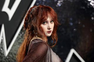 Chappell Roan with red hair and a medieval-inspired outfit poses on a glamorously lit background