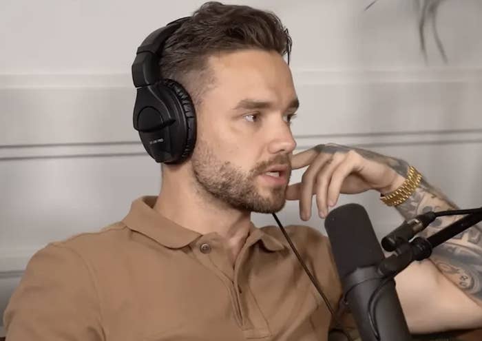 Liam Payne with short dark hair and a beard wearing headphones and a brown polo shirt, speaking into a microphone, appears to be in a podcast setting