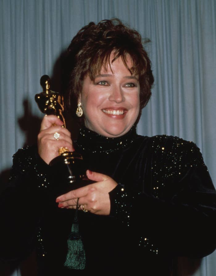 Kathy Bates holding her Oscar, smiling, wearing a sparkly outfit