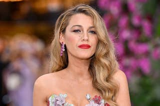 Blake Lively at a formal event, wearing a strapless gown adorned with floral embellishments and matching floral earrings. Her hair is styled in soft waves