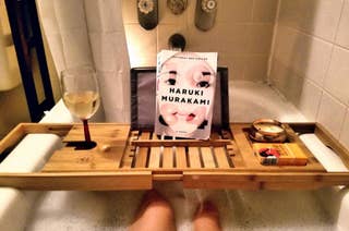 A bathtub with a wooden tray holding a glass of wine, a book titled 